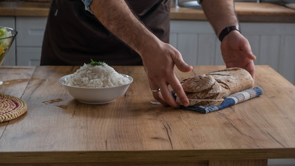 Caucasian man moves bread on a table with rice bowl in background. 