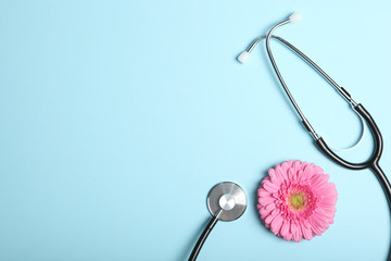 Gerbera and stethoscope on a colored background top view. Symbol of women's health and gynecology. - obrazy, fototapety, plakaty