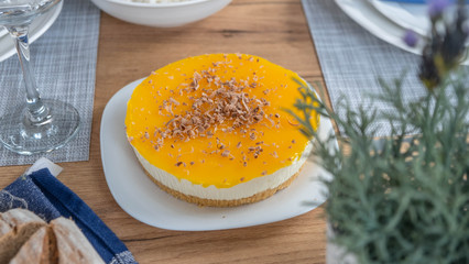 Yellow cheesecake with chocolate on top served on a table with rosemary in the background