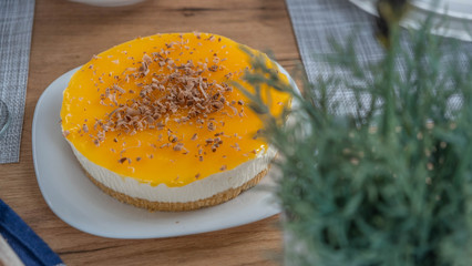 Yellow cheesecake with chocolate on top served on a table with rosemary in the background