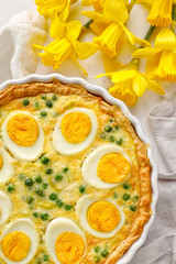 Easter tart quiche with eggs and green peas in casserole dish, close up