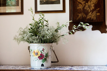 Wildflowers and willow branches stand in a white metal bucket in a village house