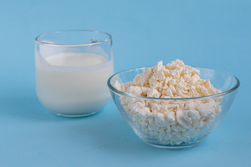 Fresh cottage cheese in a transparent bowl with a spoon with a glass of kefir on a blue background. Fermented foods. Good bacteria for health.