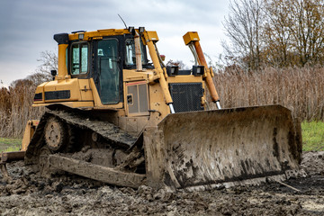 Obraz na płótnie Canvas Dirty bulldozer standing in the mud. Autumn construction site with working machines.