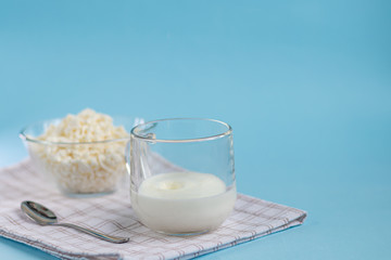 Fresh cottage cheese in a transparent bowl with a spoon and a glass in which a stream of kefir is poured on a blue background. Fermented foods. Good bacteria for health.