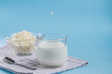 Fresh cottage cheese in a transparent bowl with a spoon and a glass in which a stream of kefir is poured on a blue background. Fermented foods. Good bacteria for health.