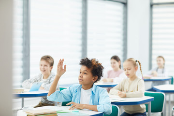 Horizontal portrait of smart African American middle school student raising his hand to give answer in class, copy space