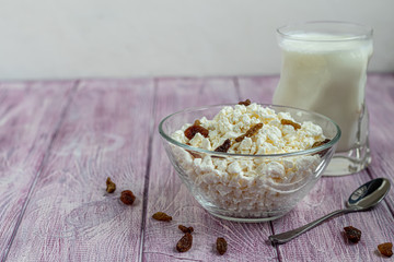 Fresh cottage cheese in a transparent bowl with raisins. In the background is a glass of kefir. Fermented foods. Good bacteria for health. Light background.