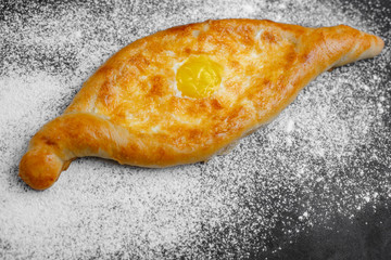 Khachapuri with egg and cheese. Georgian cuisine. On an old black background with flour and a rag. Free space for text. The view from the top. Side view.