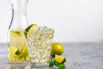 Glasses are filled with ice and cold green tea. Garnished with lime slices and a sprig of mint. On a light background.