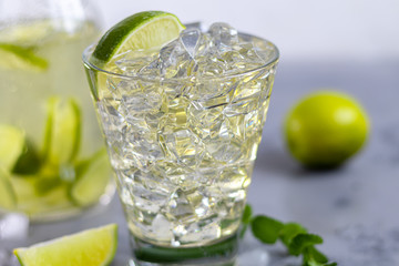 Glasses are filled with ice and cold green tea. Garnished with lime slices and a sprig of mint. On a light background.