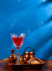 still-life. Red drink in a crystal glass. Copper dishes. On a blue background in the morning sun