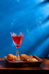 still-life. Red drink in a crystal glass on a wooden plate. On a blue background in the morning sun