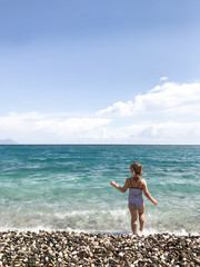 child in striped swimsuit on sea, view from back.