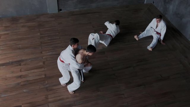 Brave powerful asian guy fighting alone against three strong warriors in white kimono. He perform active martial tricks and makes forceful attack. Slow motion and rapid. Top view.