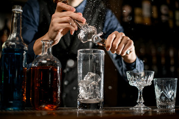 Close-up how man with special device breaks pieces of ice to make a cocktail.