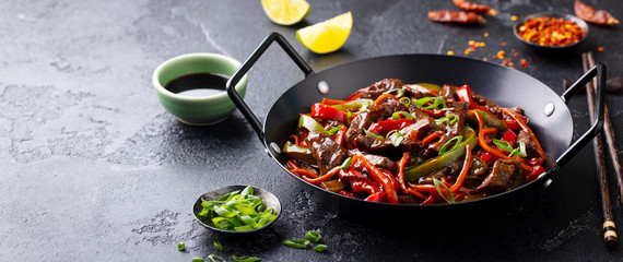 Beef and vegetables stir fry in a pan. Grey background. Copy space.