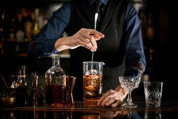 Professional bartender stirs cold cocktail with spoon