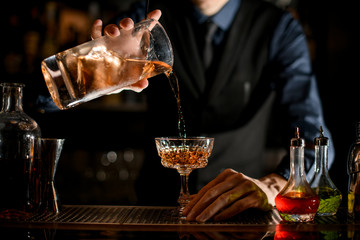 Close-up how bartender pours a ready-made cold brown cocktail into wineglass.