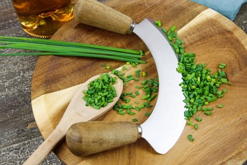 Preparation of herbs for meal: isolated brown wood cutting board with chef´s mincing knife,...