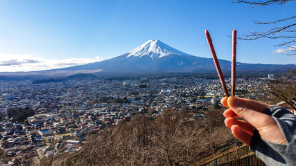 A hand holding two chocolate sticks, making a V-shape, with a distant view on Mt Fuji in Japan on a...