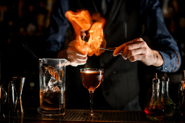 Professional man at the bar burns slice of citrus for cocktail.