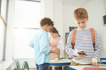 Middle school students standing in classroom using their smart phones during break, copy space
