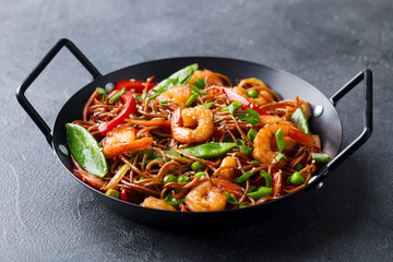 Stir fry noodles with vegetables and shrimps in black iron pan. Slate background. Close up.