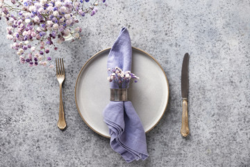 Easter table setting with grey plate and violet decor on grey stone table. Top view.