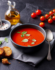 Tomato soup with basil in a bowl. Dark grey background.