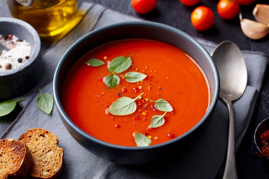 Tomato soup with basil in a bowl. Dark background. Close up.