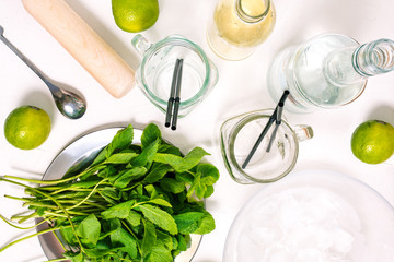 Cooking alcoholic mojito. Ingredients for a fresh summer cocktail on the table. Rum, syrup and empty cocktail jars with straws. Flat lay, top view.