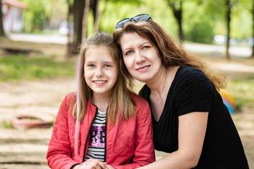 Middle-aged woman hugs her teenage daughter and they smile and relax together after serious talk about teenage issues