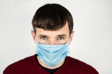 A man with a medical mask on his face on a light background, a man is afraid of getting sick, he has frightened eyes