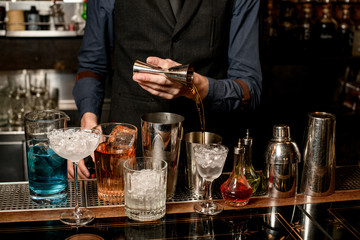 bartender pours the ingredients for the cocktail into the shaker from the beaker.