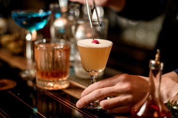 close-up bartender decorates wineglass of cocktail with small rose