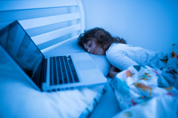 Small 11 year old girl sleeping next to a laptop - insomnia and addiction to internet in modern generation children. - obrazy, fototapety, plakaty