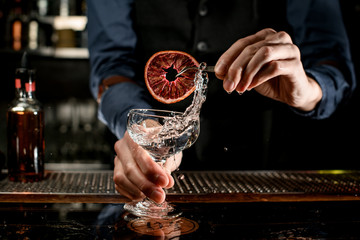 splashing drink in glass decorated with slice of citrus by barman