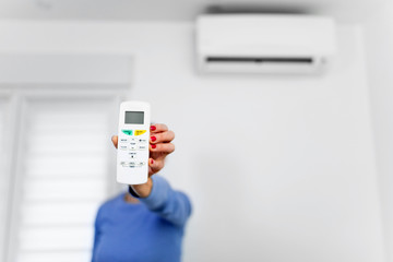 Woman holding a remote of a modern airconditioner unit at home.