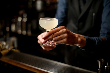 Fototapeta na wymiar bartender holding white cocktail in glass over the bar