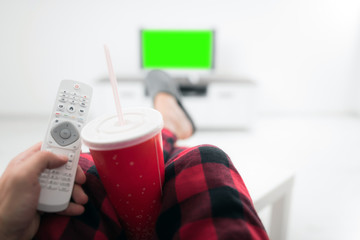 Man drinking soda juice and looking at TV with legs on the table in living room. Chroma key green screen.