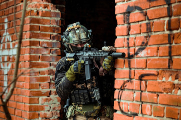 Closeup military man in black uniformaims aims at the sight machinegun. Soldier between brick walls.