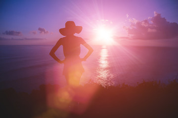 Silhouette of a woman with tropical sunset above the ocean.