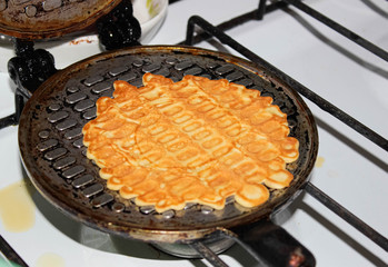 Delicious sweet waffles for dessert are baked on the stove in a waffle iron.