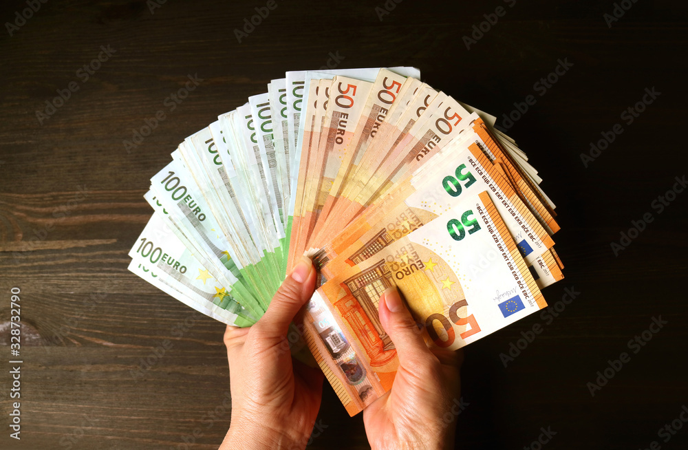 Wall mural bundle of euro banknotes in female's hand against dark brown wooden background