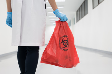 Scientist wearing blue gloves and red bag with bioharzard sign.A woman worker hand holding red...