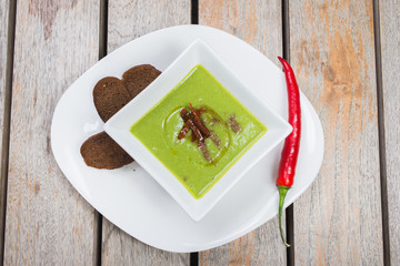 Green vegetarian broccoli cream soup with rye crackers on a wooden table in a restaurant or cafe.