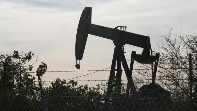 Industrial urban landscape. La Brea Inglewood in Los Angeles. Well pump jack operating behind the fence. Drilling rig extract crude oil. Oil mining machine with working piston. Oil and gas industry.