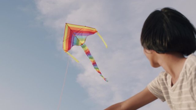 Happy Asian girl is playing rainbow kite flying on the blue sky joyful and enjoying in the summer at outdoor sunlight. Summer lifestyle concept 