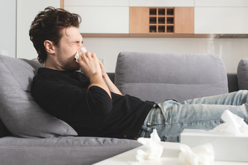 Sick man lying on sofa and blowing nose